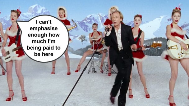 Bill Nighy wearing a suit and singing with women dressed in Christmas outfits around him from Love Actually.