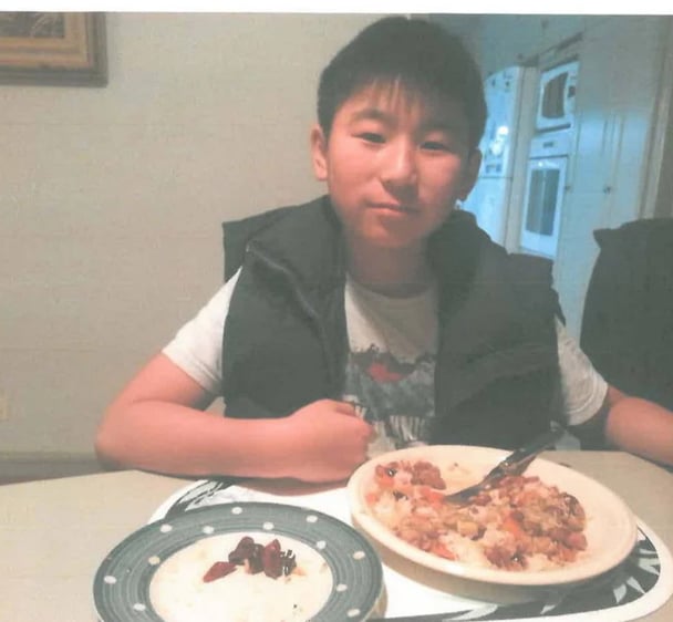 Pre-teen boy sits at a table with a meal in front of him.