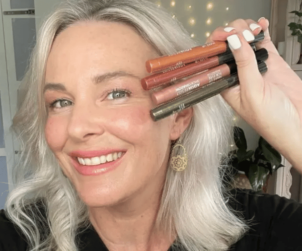 Smiling woman holding up Make Up For Ever eyeshadow sticks.