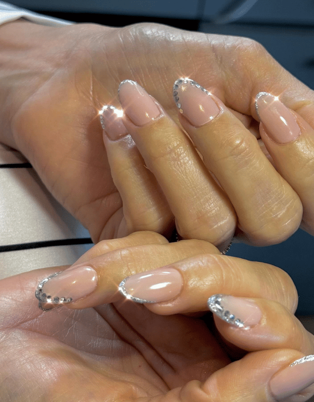 Close up of Jessica Alba's hands, featuring a French manicure with silver jewels on the tips of nails, shaped in a nail crown design.