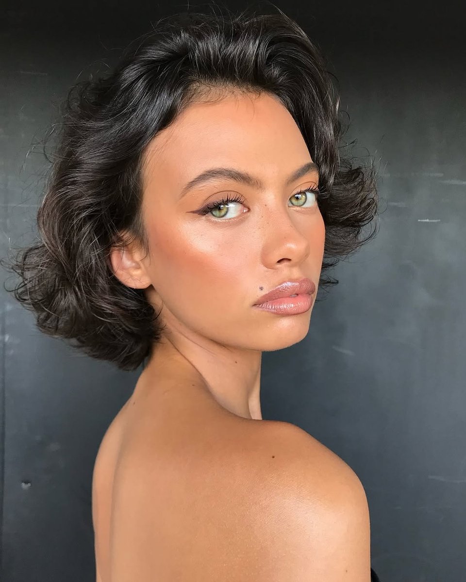 A model poses for camera wearing a short brunette bob and brown eyeliner wing.