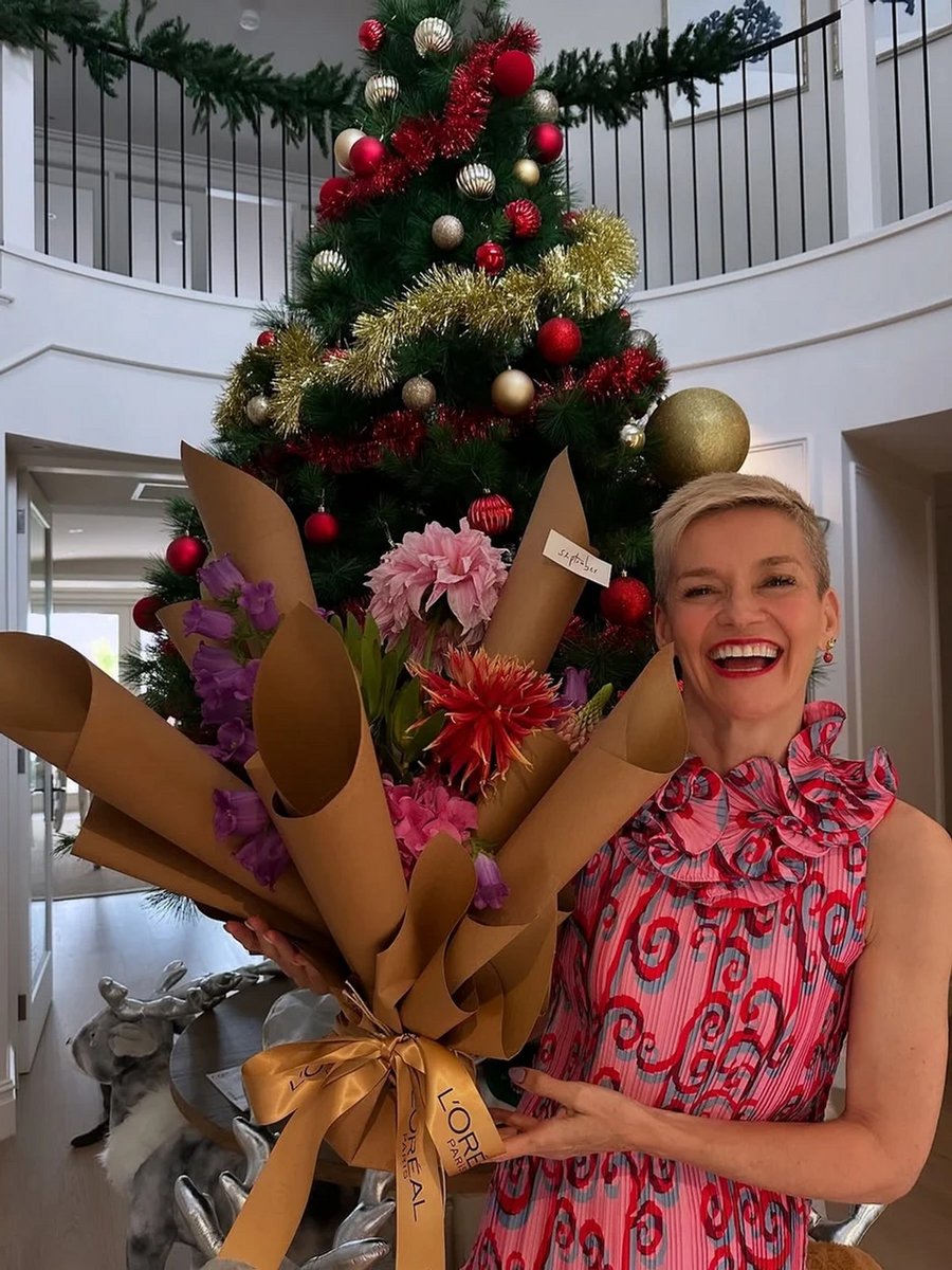 Jess Rowe holding a bouquet of flowers in front of a large Christmas tree. 