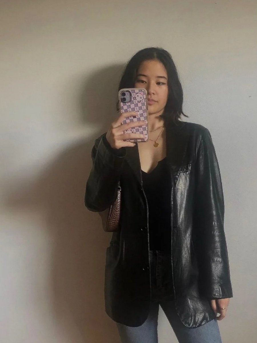 Girl in a leather jacket taking a photo.