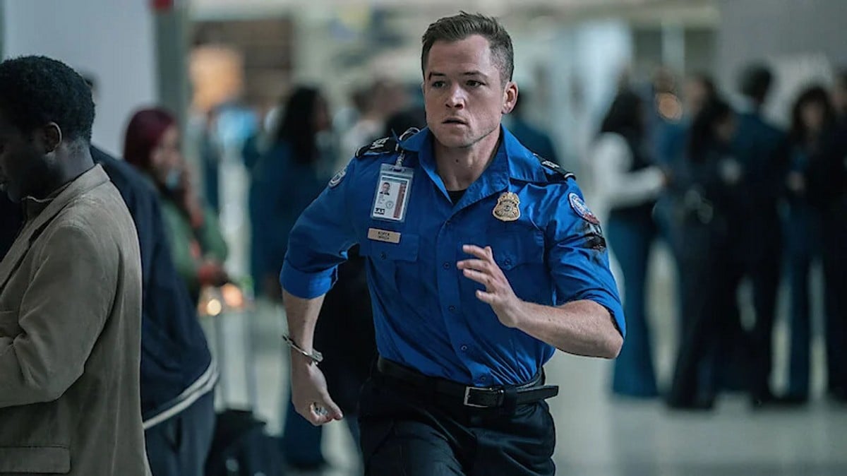 Taron Egerton in a TSA uniform running through the airport from a scene in Carry On. 