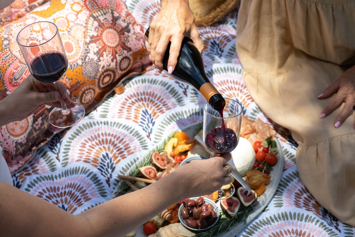 Woman pouring champagne at picnic over a Charcuterie board.