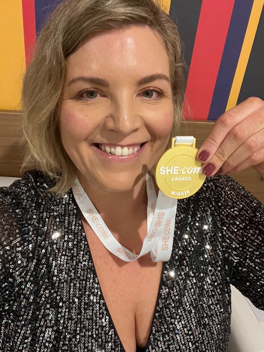 Woman with a blonde bob weating a sparkly v-neck top holding a gold medal around her neck.