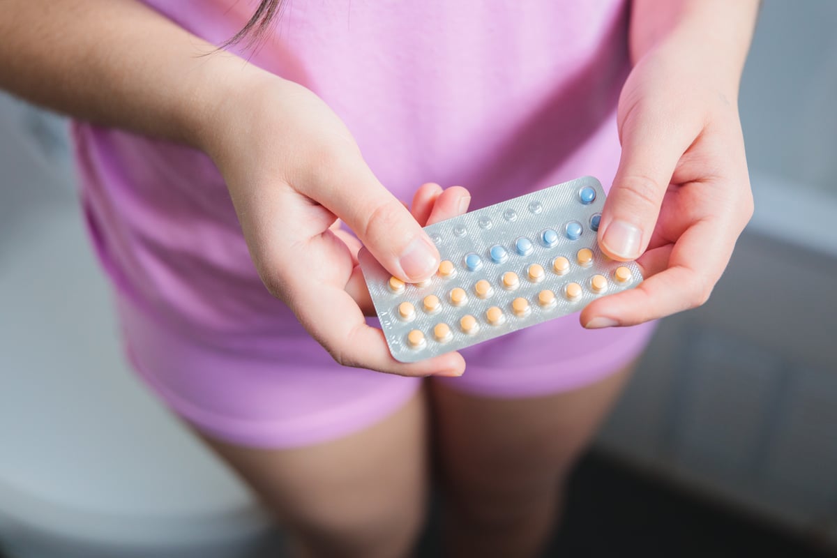 A woman wearing a pink shirt holds her contraceptive pills in the bathroom.