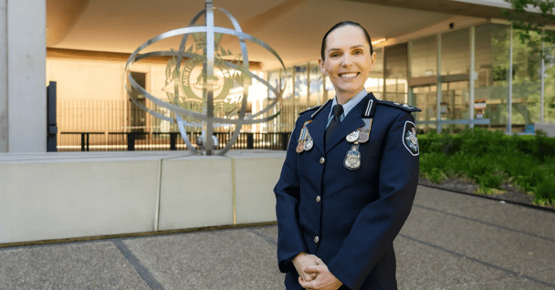 AFP Acting Commander Amelia McDonald standing smiling, in full uniform featuring badges, outside of the AFP building.