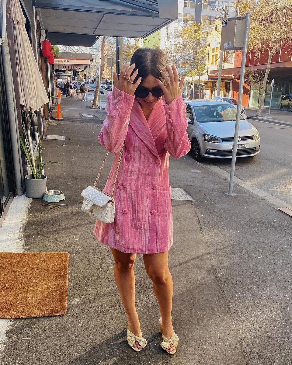 Tamara Holland wears a pink blazer dress and gold heels in a photograph taken outside a city venue.