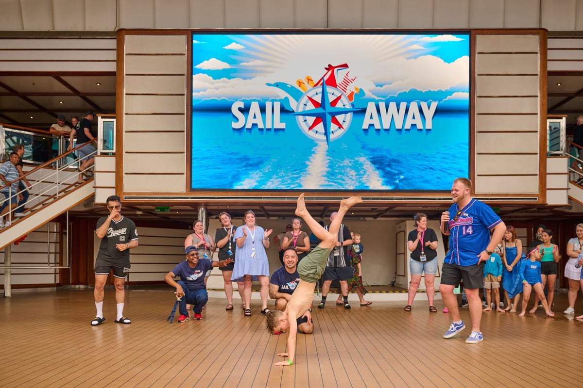 Boy dancing, doing a handstand on a cruise ship dance competition as a group of people around him cheer him on.