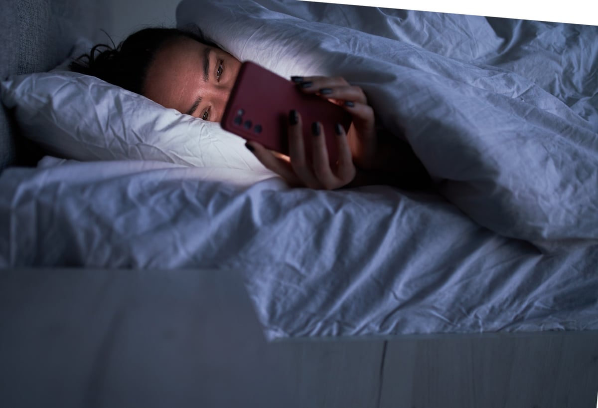 woman on smartphone in bed trying to sleep.