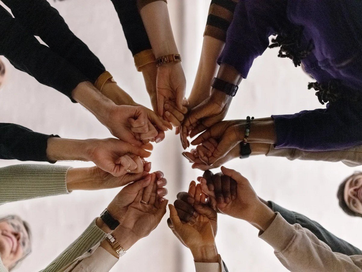 Low angle view of group of people in circle and holding their fists together during a group therapy session. People with fist put together during support group session.