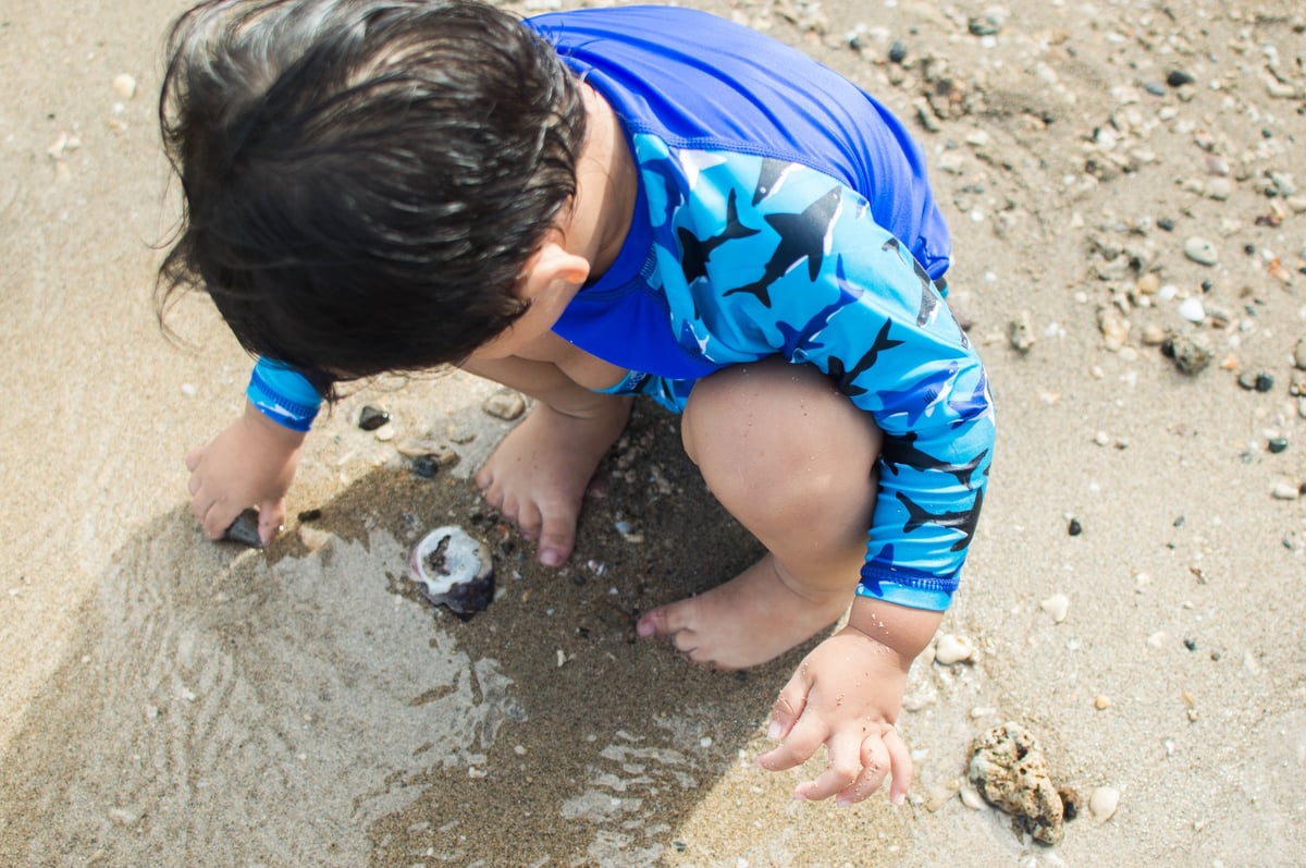 Boy playing in the sand in his swimmers, which are blue and covered in a shark motif.