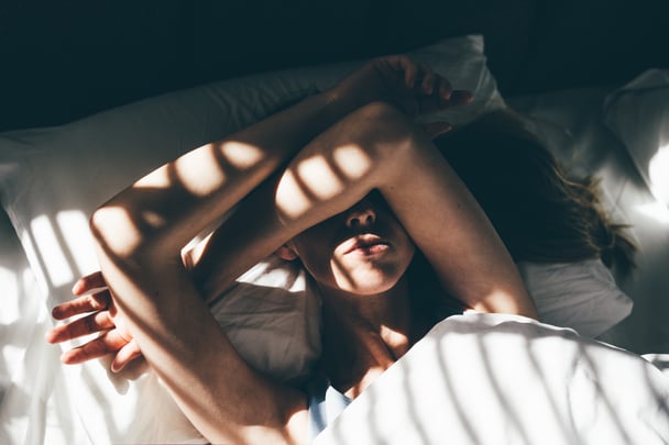 woman covering eyes from light in bed