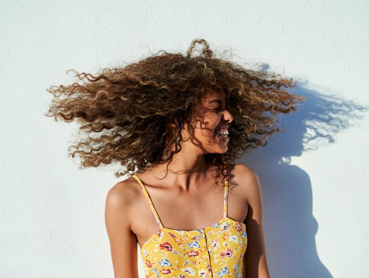 Portrait of wo.man moving her curly hair in front of white wall