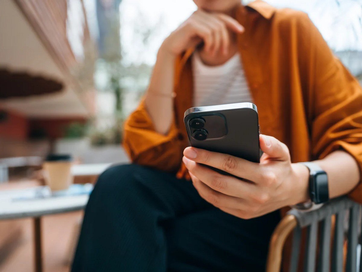 Close up shot of a young Asian woman using smartphone while sitting in an outdoor cafe and drinking coffee