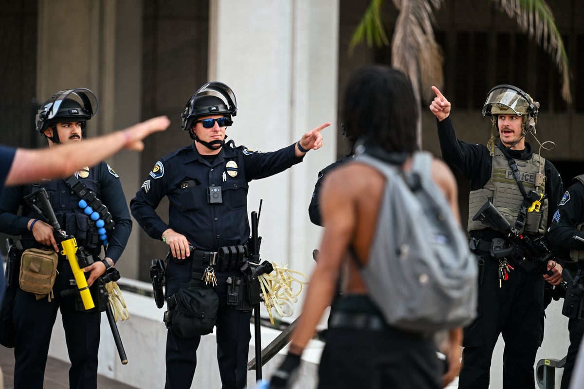 An LAPD officer draws his sidearm while confronting rioters after a protest against local ICE raids escalated into violence, in Los Angeles.