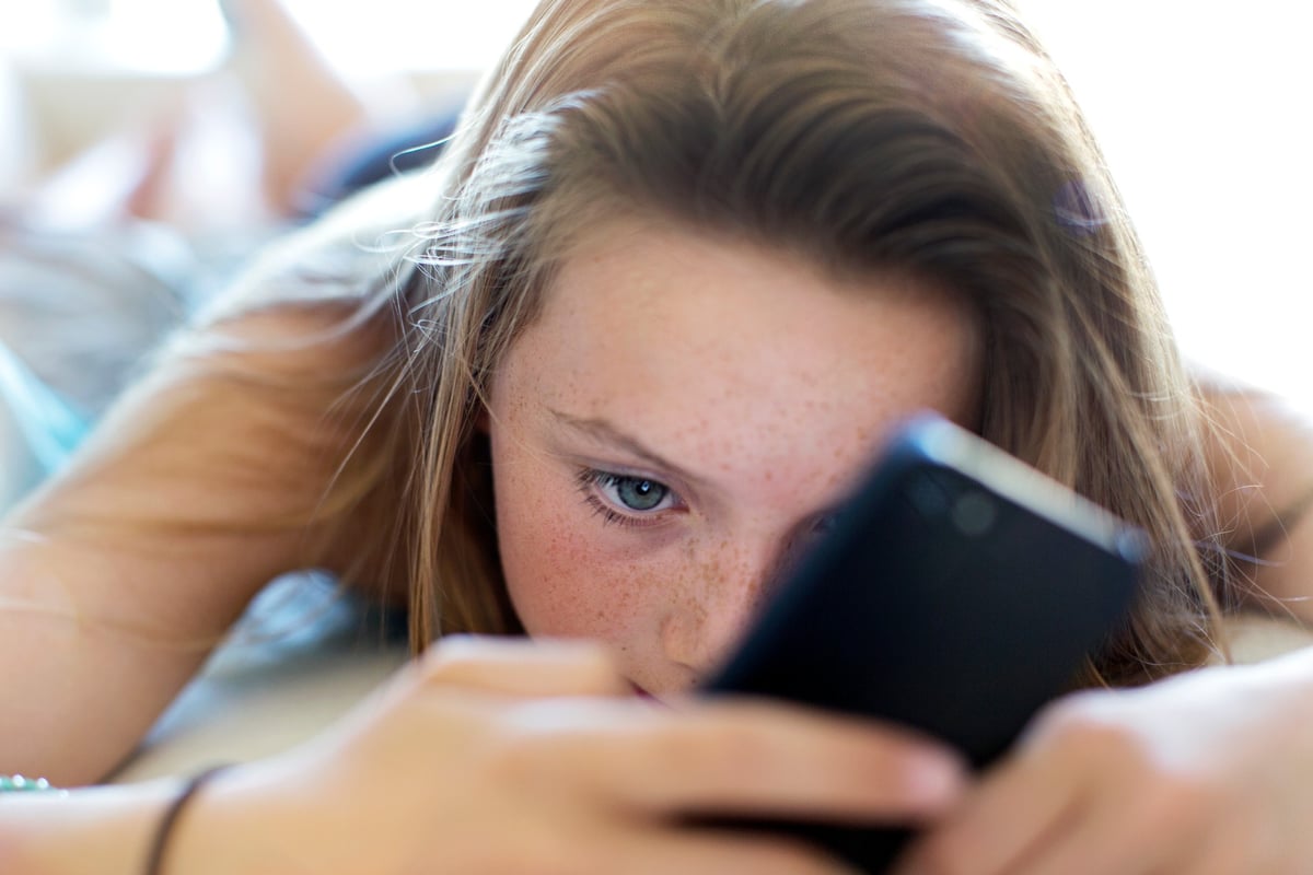 A teenage girl scrolls on her phone while laying down.