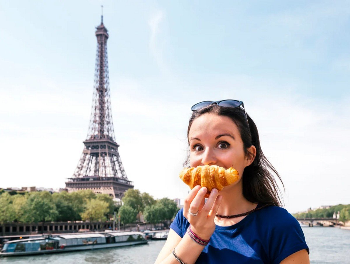 France, Paris, staring woman with croissant in front of Seine river and Eiffel Tower