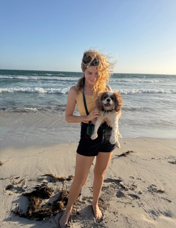 Megan Marx in a bikini on the beach holding her dog.