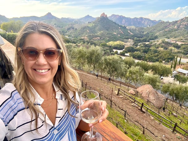 Selfie of Sasha holding a glass of wine at a vineyard.