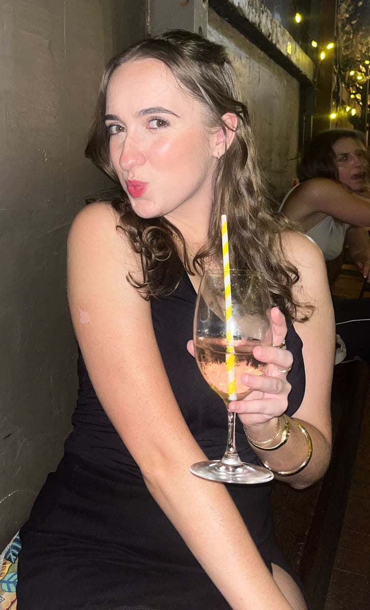 A young woman wearing a black dress and holding a drink while posing for the camera on a night out. 