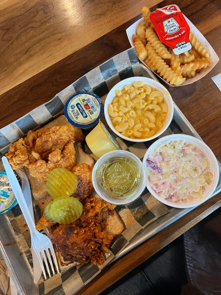 A plate of Prince's Hot Chicken featuring four chicken tenders on white bread, pickles, coleslaw and mac and cheese.
