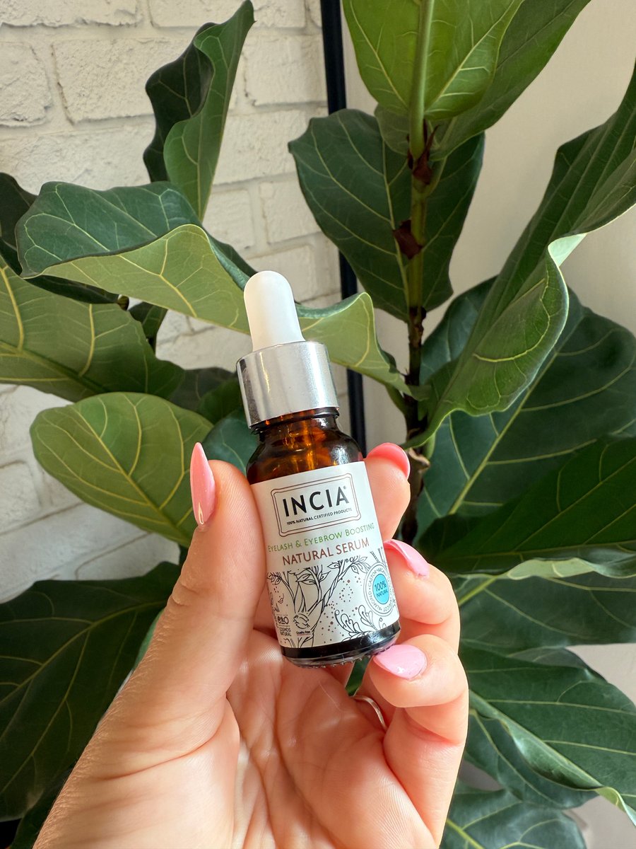 A woman's hand holds a bottle of INCIA Natural Eyebrow and Eyelash Care Serum