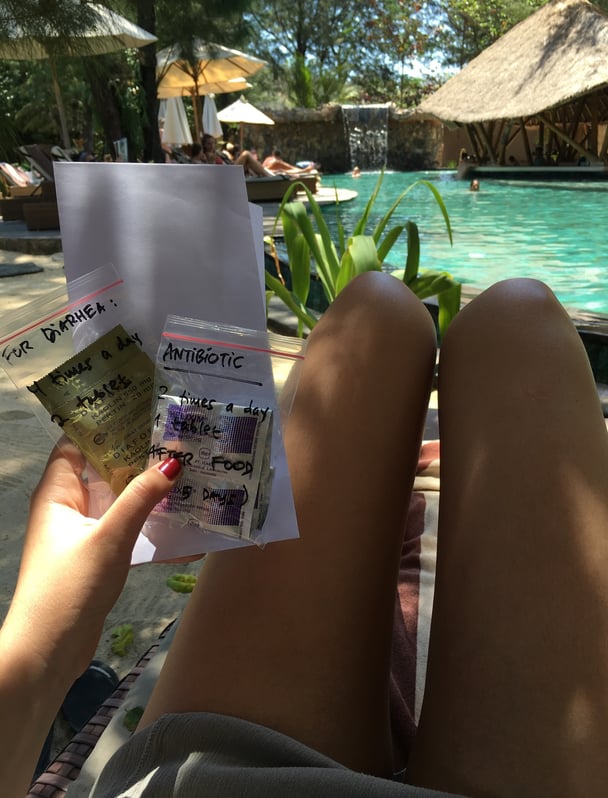 Paige sitting by a pool at a villa in Bali holding medication for diarrhea.