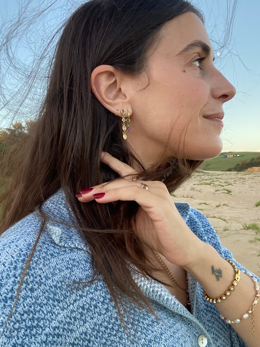 Author wears layered gold earrings with coloured gemstones.