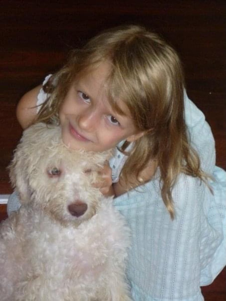 A young girl cuddles a fluffy white puppy.