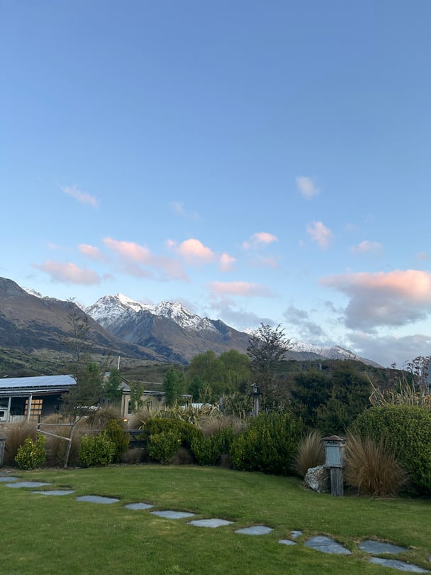 A grassy area with a stone footpath, and snow-capped mountains in the background.