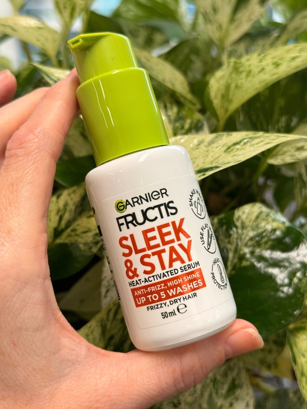 A bottle of Garnier Fructis Keratin Sleek & Stay Serum on a background of green leaves.