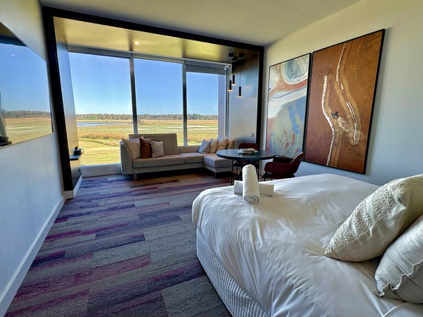 Inside the bedroom with a bed and reading bench overlooking a large window with a view of wetlands.