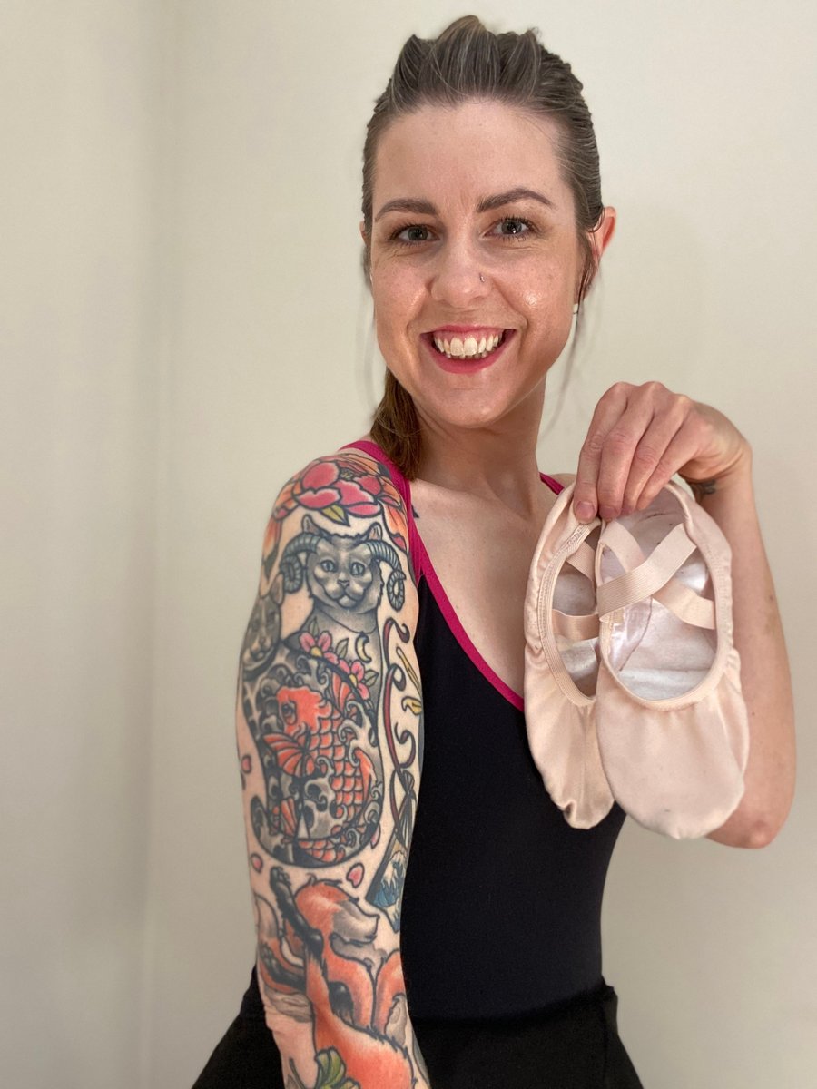 Smiling woman poses holding a pair of ballet slippers.