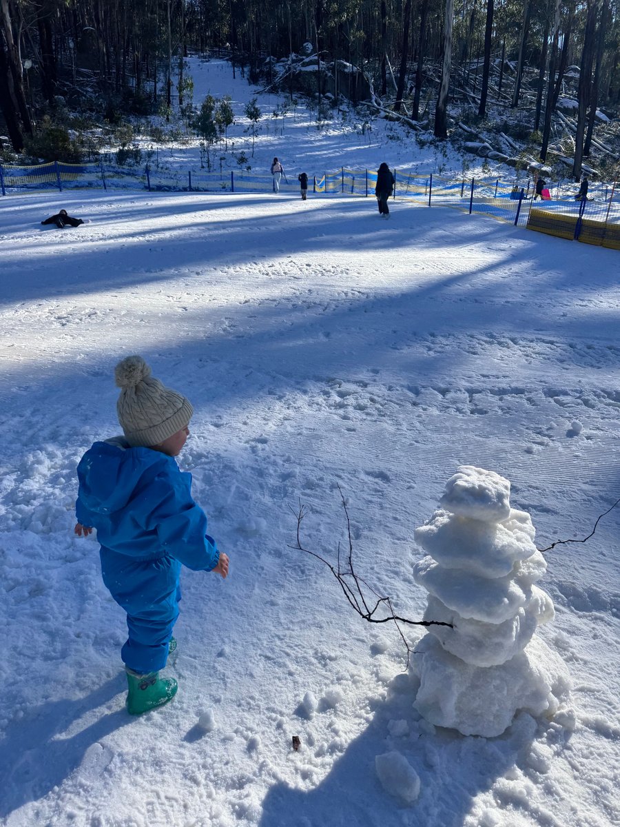 Little boy in thick clothes stands in the snow with a snowman.
