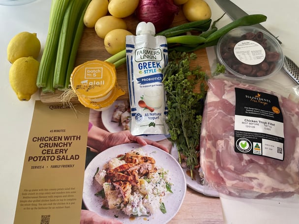 A QuiteLike recipe card and some raw ingredients laid out on a kitchen bench including chicken thigh fillets, lemons, celery, potatoes and a greek yoghurt pouch.