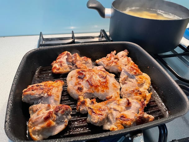 Chicken thigh fillets cooking on a cast iron grill pan.