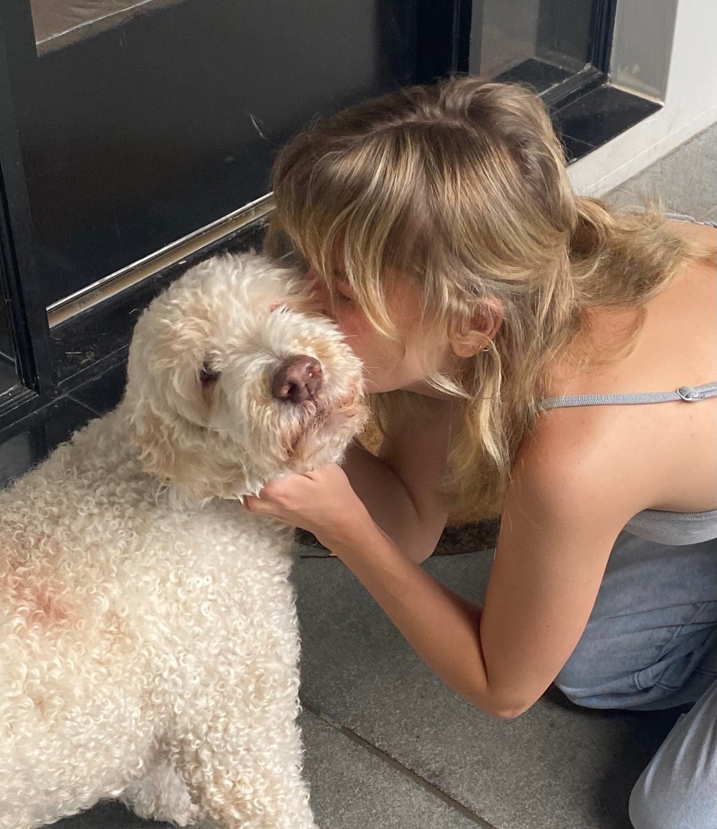 A young woman kisses a fluffy white dog on the cheek.