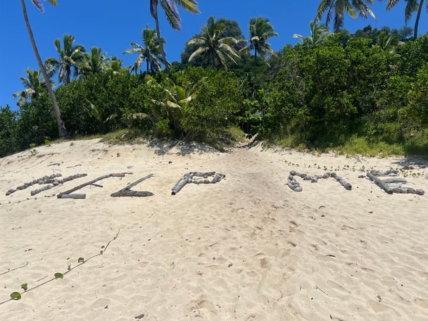 'help me' spelled out in rocks and tree brances on a sandy beach