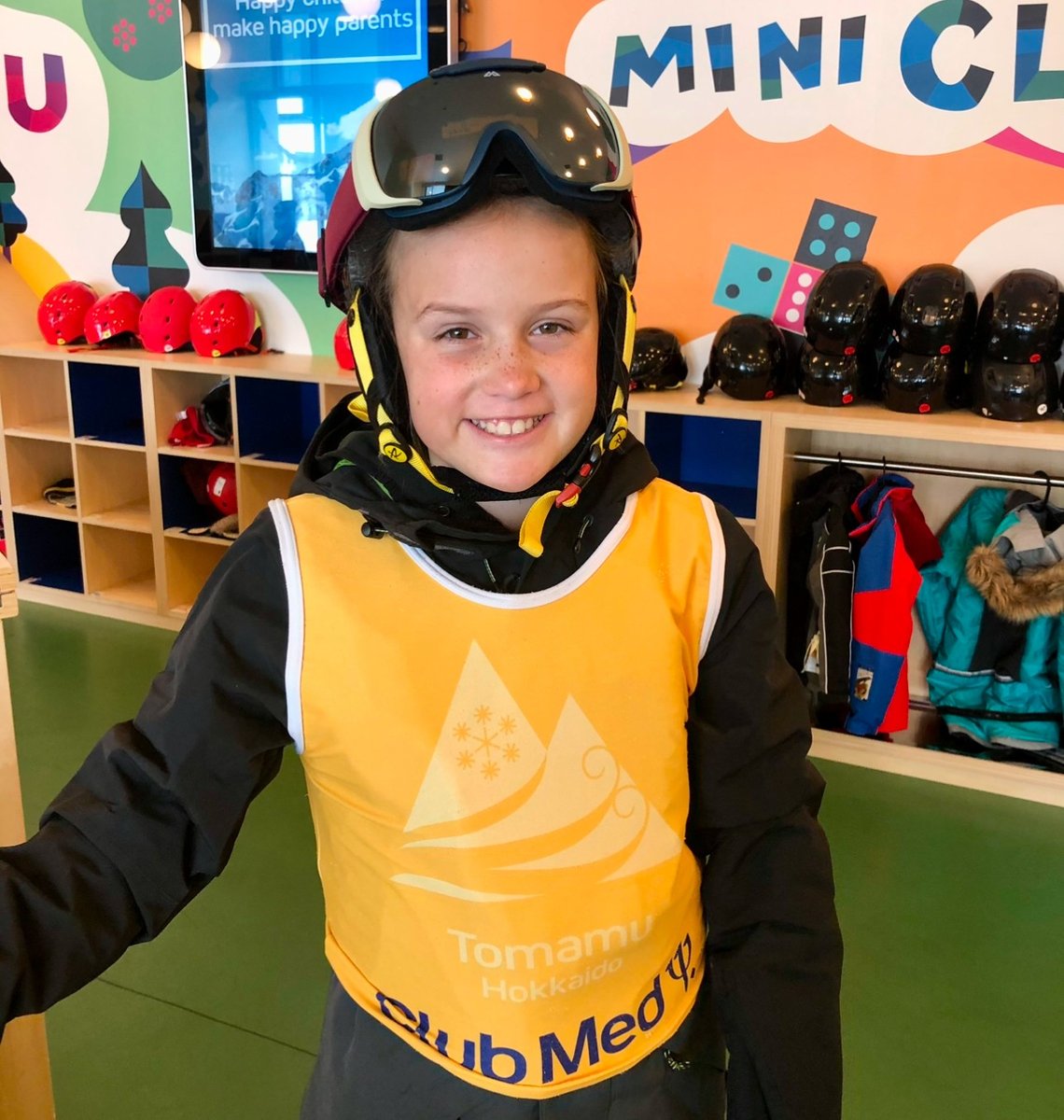 A smiling young girl stands in ski gear, looking excited and ready for her lesson.