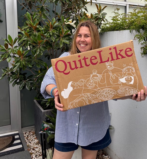 The writer standing at her front door holding her QuiteLike delivery in a branded cardboard box.