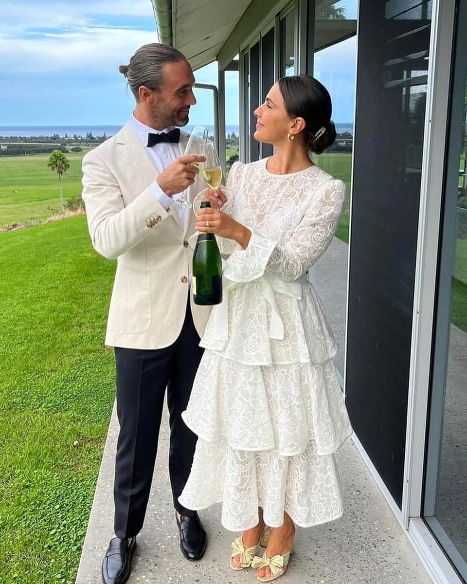 A wedding photo featuring a couple sharing a glass of champagne, with a background of green hills and the ocean.