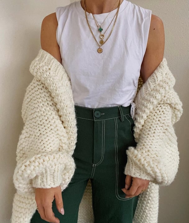 A fashion image featuring chunky cardigan, tank top and stacked necklaces.