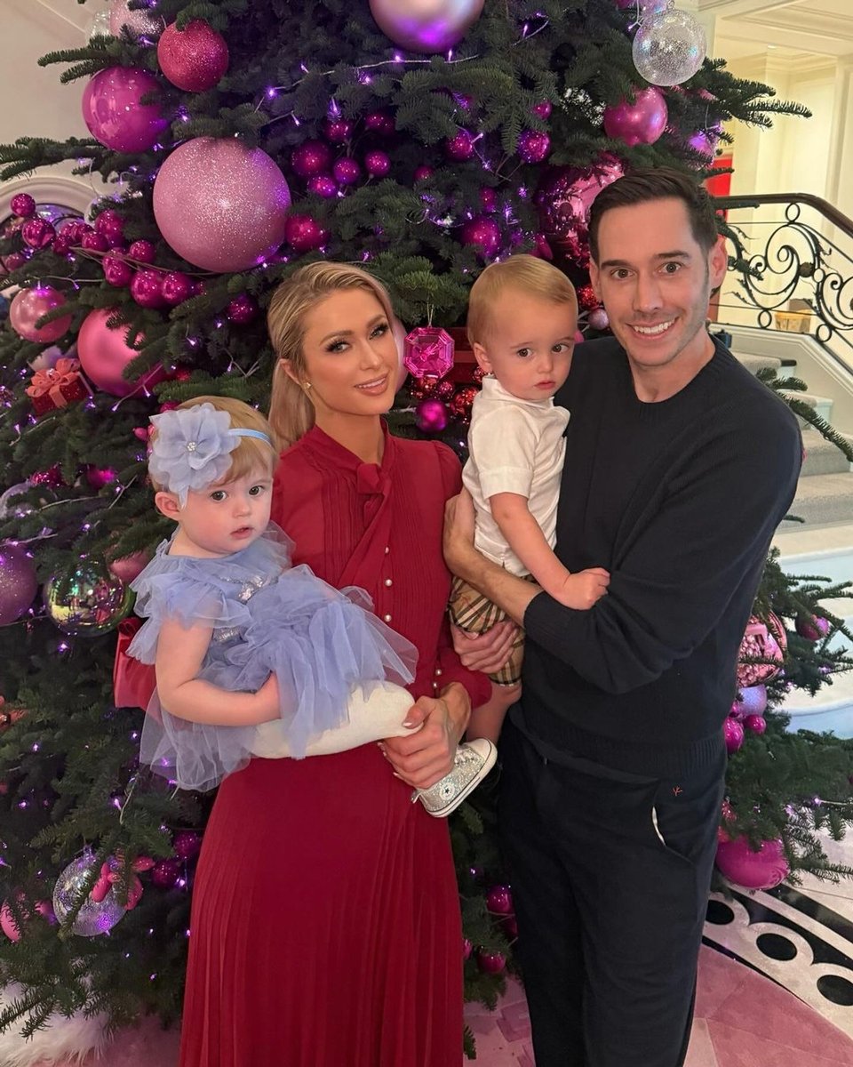 Paris Hilton, husband Carter Reum and their children, Phoenix and London, pose in front of their Christmas tree, which is decorated with large pink baubles.