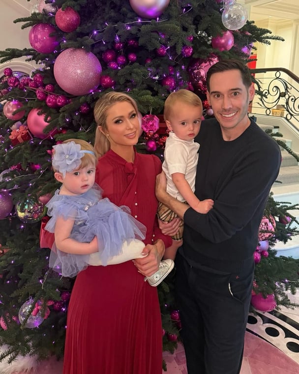 Paris Hilton, husband Carter Reum and their children, Phoenix and London, pose in front of their Christmas tree, which is decorated with large pink baubles.