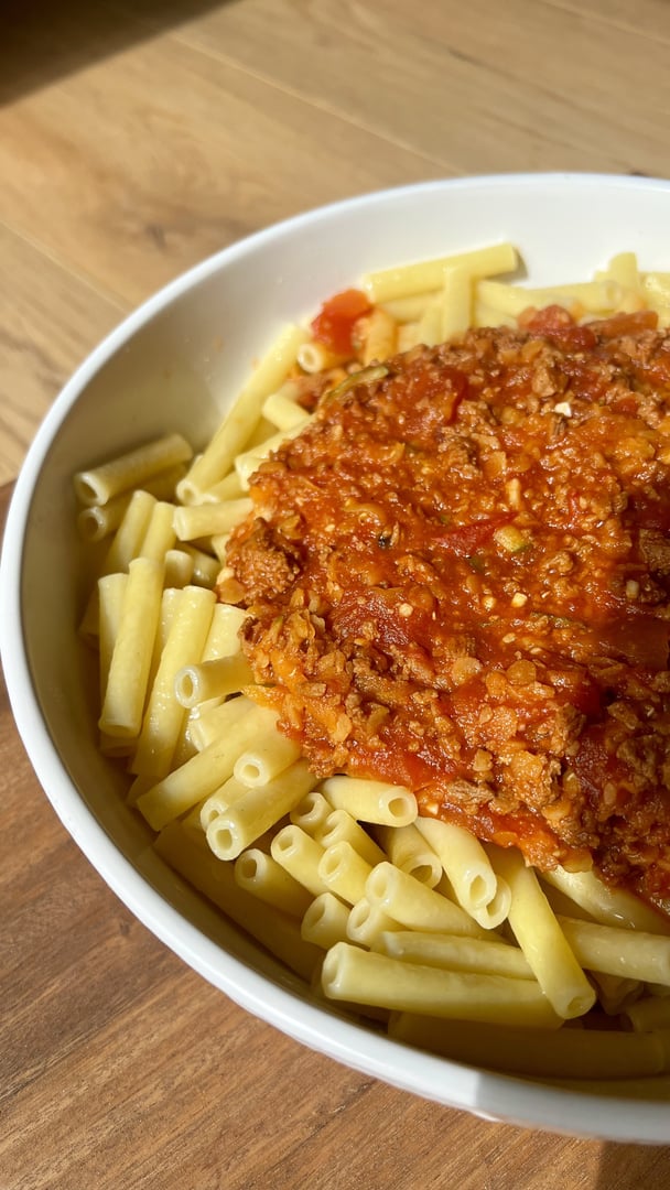 A bowl of pasta topped with rich, chunky hidden-veg bolognese sauce on a light pink surface.
