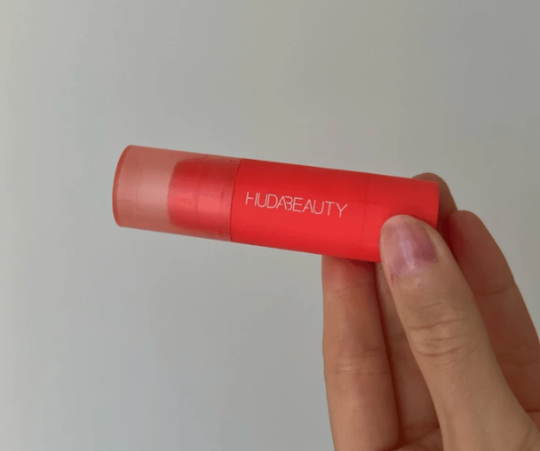 Woman's hand holding Huda Beauty Cheeky Tint Blush Stick.