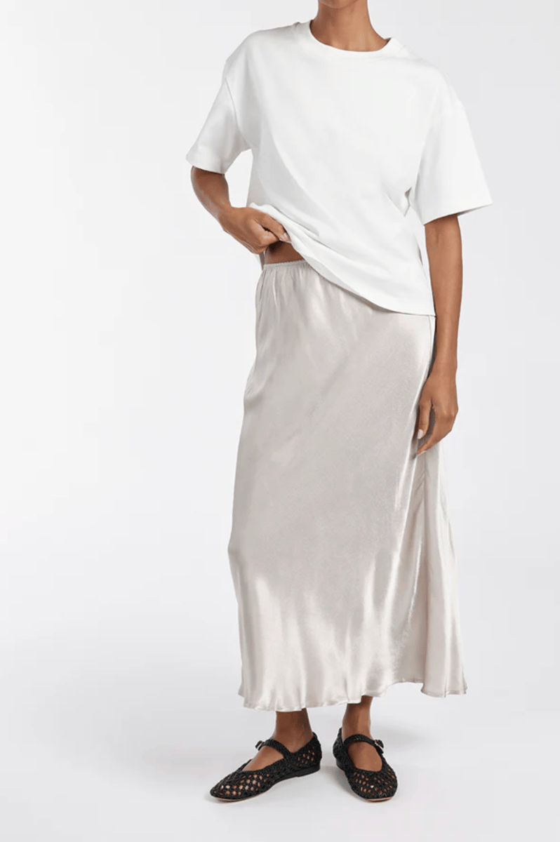 A model wears a silky white midi skirt and black woven ballet flats.