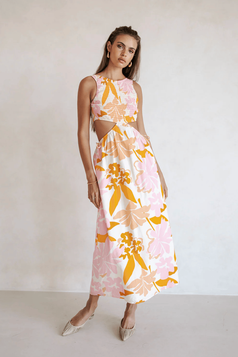 A model wears a sleeveless midi dress with a splashy pink and orange floral print.